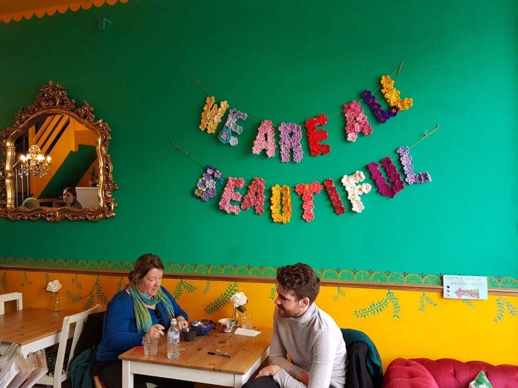 Picture of the colourful upstairs seating ares with 2 people sitting and behind saying 'we are beautiful'